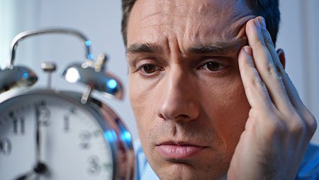 Мужчина держится за голову на фоне будильника